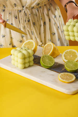 Female hands about to cut a bright green bubble candle surrounded by lemon and lime halves, fresh thymeの写真素材