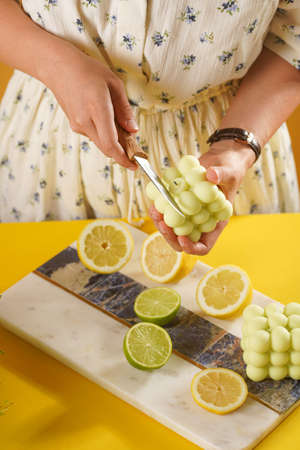 Female hands about to cut a bright green bubble candle surrounded by lemon and lime halves, fresh thymeの写真素材