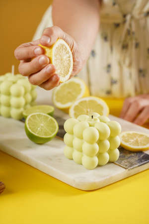 Female hands pressing lemon juice on a bright green bubble candle surrounded by lemon and lime halves, fresh thymeの写真素材
