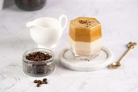 glass with trendy korean beverage dalgona coffee latte - whipped instant coffee, sugar and hot water and milk layers on a marble board, white surfaceの写真素材