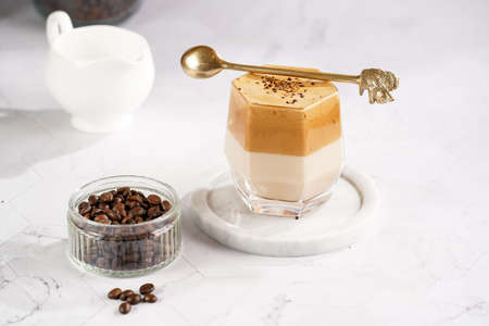 glass with trendy korean beverage dalgona coffee latte - whipped instant coffee, sugar and hot water and milk layers on a marble board, white surfaceの写真素材
