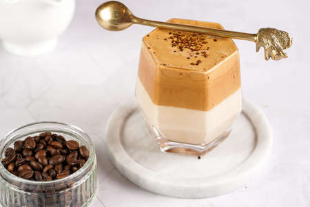 glass with trendy korean beverage dalgona coffee latte - whipped instant coffee, sugar and hot water and milk layers on a marble board, white surfaceの写真素材