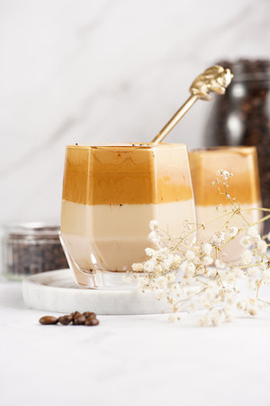 Two glasses with trendy korean beverage dalgona coffee latte - whipped instant coffee, sugar and hot water and milk layers on a marble board, white surfaceの写真素材