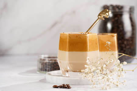 Two glasses with trendy korean beverage dalgona coffee latte - whipped instant coffee, sugar and hot water and milk layers on a marble board, white surfaceの写真素材