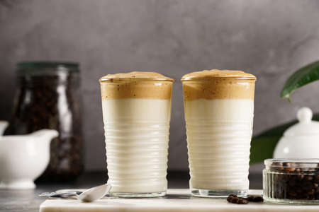Two glasses with trendy korean beverage dalgona coffee latte - whipped instant coffee, sugar and hot water and milk layers on a marble board, gray surfaceの写真素材