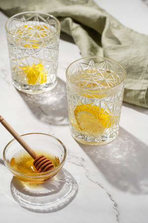 Two glasses with water and lemon, honey in the morning light - breakfastの写真素材