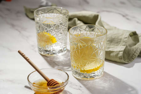 Two glasses with water and lemon, honey in the morning light - breakfastの写真素材