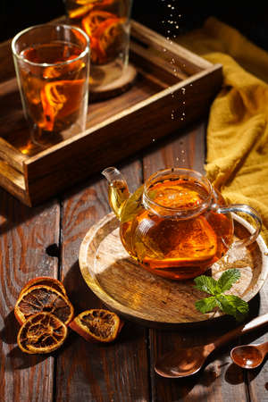 Sifting black tea into a transparent tea pot filled with black tea, oranges and mint on a wooden surfaceの写真素材