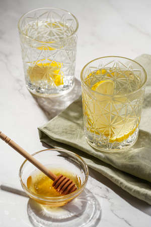 Two glasses with water and lemon, honey in the morning light - breakfastの写真素材