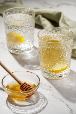 Two glasses with water and lemon, honey in the morning light - breakfastの写真素材