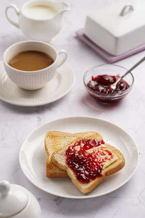 sweet breakfast - toast bread with butter and cherry jam on a white plate, cup of cappuccinoの写真素材
