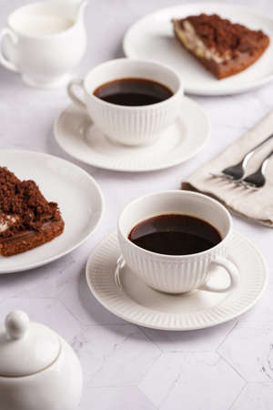 sweet breakfast - two white porcelain cups with coffee drink on a white saucer, piece of brown cakeの写真素材