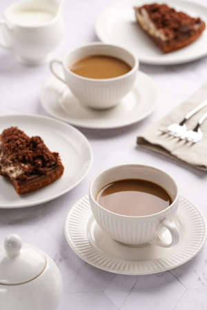 sweet breakfast - two white porcelain cups with coffee drink cappuccino with milk on a white saucer, piece of brown cakeの写真素材