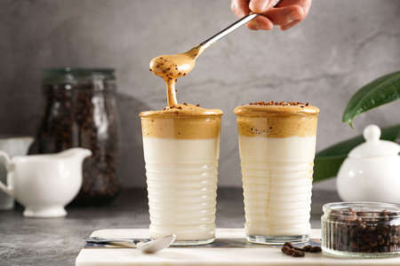 Male hand stirring trendy korean beverage dalgona coffee latte - whipped instant coffee, sugar and hot water and milk layers on a marble board, gray surfaceの写真素材