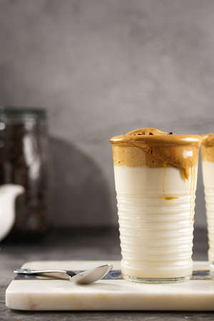 Two glasses with trendy korean beverage dalgona coffee latte - whipped instant coffee, sugar and hot water and milk layers on a marble board, gray surfaceの写真素材
