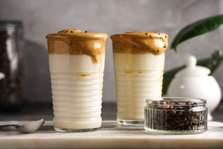 Two glasses with trendy korean beverage dalgona coffee latte - whipped instant coffee, sugar and hot water and milk layers on a marble board, gray surfaceの写真素材