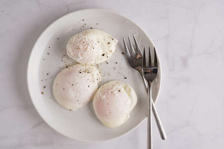 Three poached eggs on a white plate and silver colored forksの写真素材