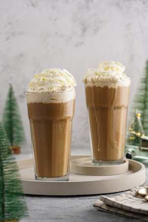 Two tall glasses with cold coffee drink frappe - iced cappuccino with whipped cream, christmas decoration and treesの写真素材