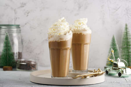 Two tall glasses with cold coffee drink frappe - iced cappuccino with whipped cream, christmas decoration and treesの写真素材