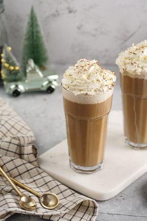 Two tall glasses with cold coffee drink frappe - iced cappuccino with whipped cream on a marble board and christmas ornaments and decorationの写真素材