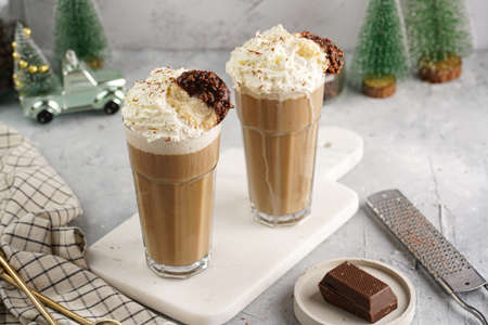 Two tall glasses with cold coffee drink frappe - iced cappuccino with whipped cream on a marble board and christmas ornaments and decorationの写真素材