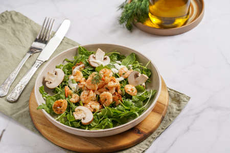 Arugula salad with shrimp and champignons, olive oil and dill on a wooden board on a white surfaceの写真素材