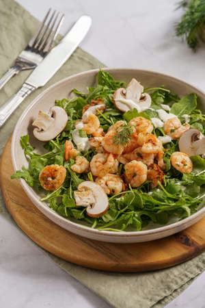 Arugula salad with shrimp and champignons, olive oil and dill on a wooden board on a white surfaceの写真素材