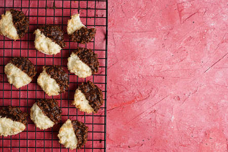 Several coconut flakes cookies dipped in chocolate on a baking rack on magenta surface, top viewの写真素材