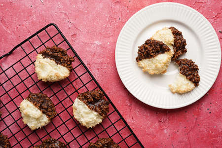 Several coconut flakes cookies dipped in chocolate on a white plate and baking rack on magenta surface, top viewの写真素材