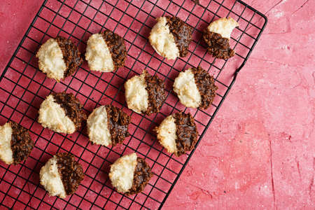 Several coconut flakes cookies dipped in chocolate on a baking rack on magenta surface, top view