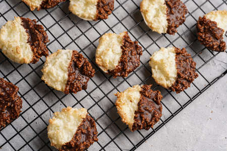 Several coconut flakes cookies dipped in chocolate on a baking rack on gray concrete surface, top viewの写真素材