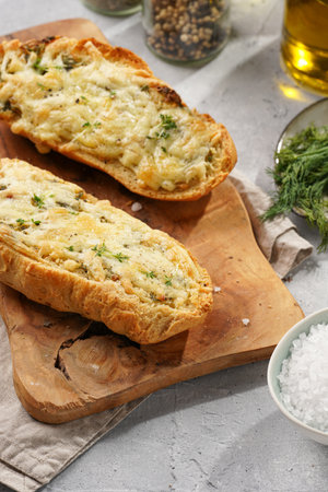 Two halves of garlic and butter bread - baguette on a wooden board, sea salt, pepper, dill and garlic cloves on a gray concrete background, top viewの写真素材