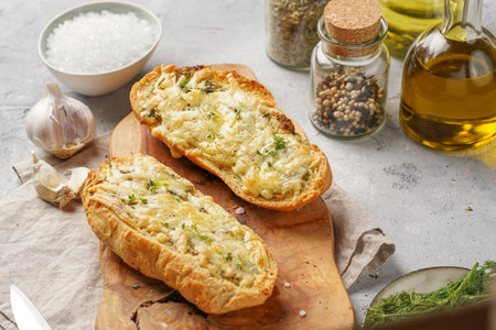 Two halves of garlic and butter bread - baguette on a wooden board, sea salt, pepper, dill and garlic cloves on a gray concrete background, top viewの写真素材