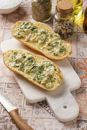 Two halves of garlic and butter bread - baguette on a marble board, sea salt, pepper, dill and garlic cloves, top viewの写真素材