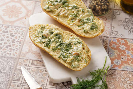 Two halves of garlic and butter bread - baguette on a marble board, sea salt, pepper, dill and garlic cloves, top viewの写真素材