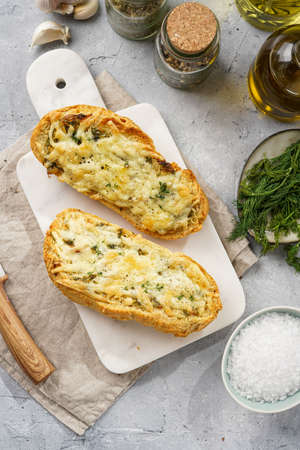 Two halves of garlic and butter bread - baguette on a marble board, sea salt, pepper, dill and...