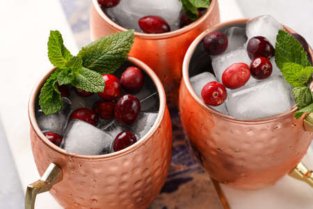 Traditional american alcoholic beverage moscow mule in copper mugs with cranberry and mint on white marble board - non-alcoholic cocktail versionの写真素材