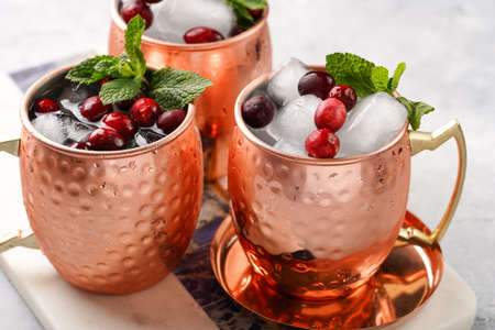 Traditional american alcoholic beverage moscow mule in copper mugs with cranberry and mint on white marble board - non-alcoholic cocktail versionの写真素材