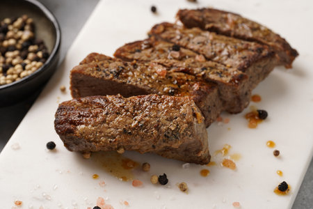 A piece of cooked beef meat steak on white marble board cut in slices, white and black peer, coarse sea saltの写真素材