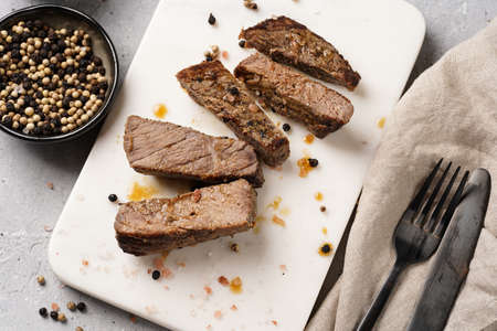 A piece of cooked beef meat steak on white marble board cut in slices, white and black peer, coarse sea saltの写真素材