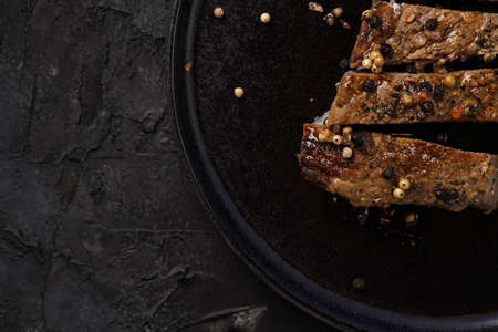A piece of cooked beef meat steak on black plate cut in slices, white and black peer, coarse sea saltの写真素材