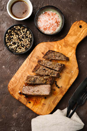 A piece of cooked beef meat steak on wooden board cut in slices, white and black peer, coarse sea salt, top viewの写真素材