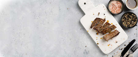 A piece of cooked beef meat steak on white marble board cut in slices, white and black peer, coarse sea salt. Top view, negative space, bannerの写真素材