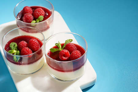 Italian dairy dessert panna cotta with raspberry jam and fresh raspberries on marble board on blue surface, negative spaceの写真素材