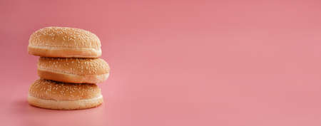 Three white wheat burger buns with sesame seeds on pink seamless surface, copy space, bannerの写真素材