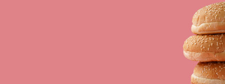 Three white wheat burger buns with sesame seeds on pink seamless surface, extreme close-up, copy spaceの写真素材