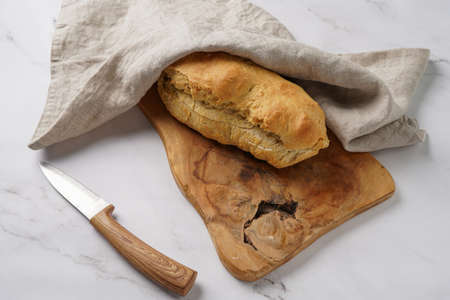 A loaf of homemade wheat bread on a wooden board on marble surfaceの写真素材