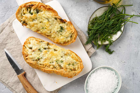 Two halves of garlic and butter bread - baguette on a marble board, sea salt, pepper, dill and garlic cloves on a gray concrete background, top viewの写真素材
