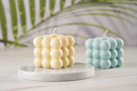 One white square bubble candle on a marble board and one blue on a tropical backgroundの写真素材