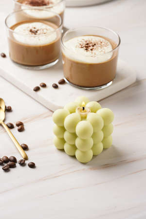 A pale green square bubble candle on a marble kitchen table among coffee beans and sweet dessert - chocolate mouseの写真素材